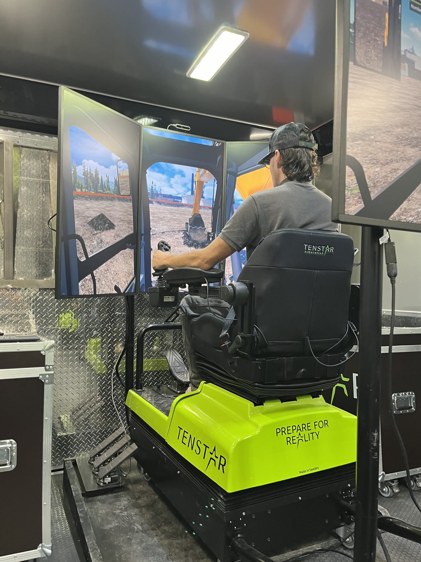 Operator practicing excavator controls on a multi-screen heavy equipment simulator