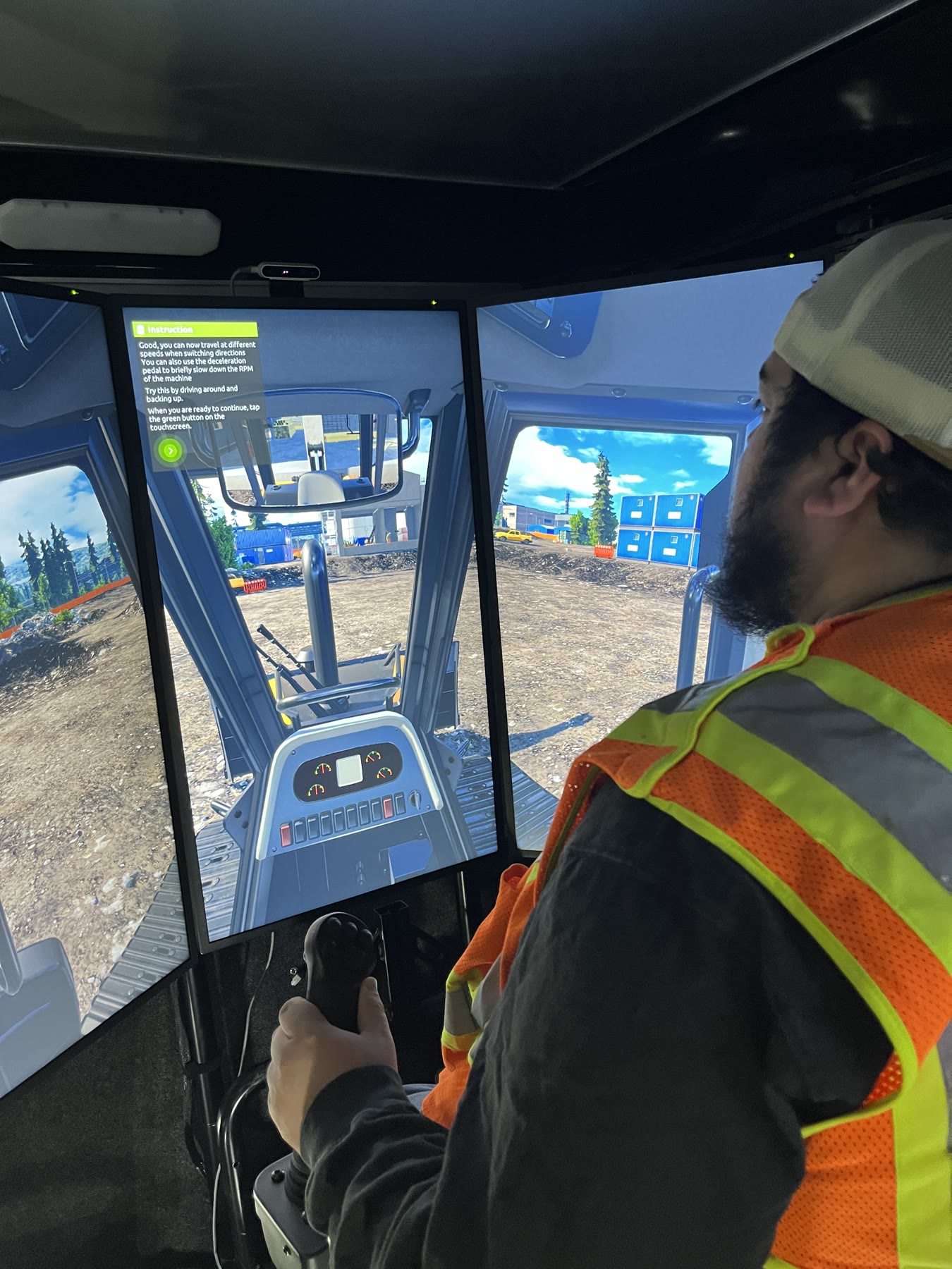 Operator practicing excavator controls on a multi-screen heavy equipment simulator